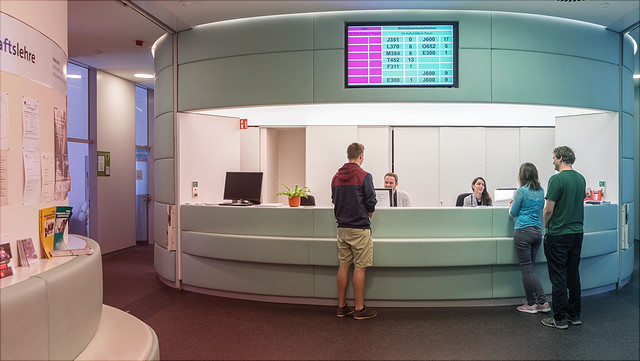 teaser-studienkoordination Am Tresen des Studienbüros der Betriebswirtschaftslehre stehen drei Personen. Über dem Tresen ist ein Monitor mit Aufruf- und Raumnummern befestigt.