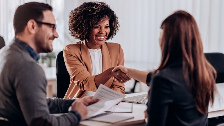 ein Mann und zwei Frauen, die Hände schütteln, an einem Tisch